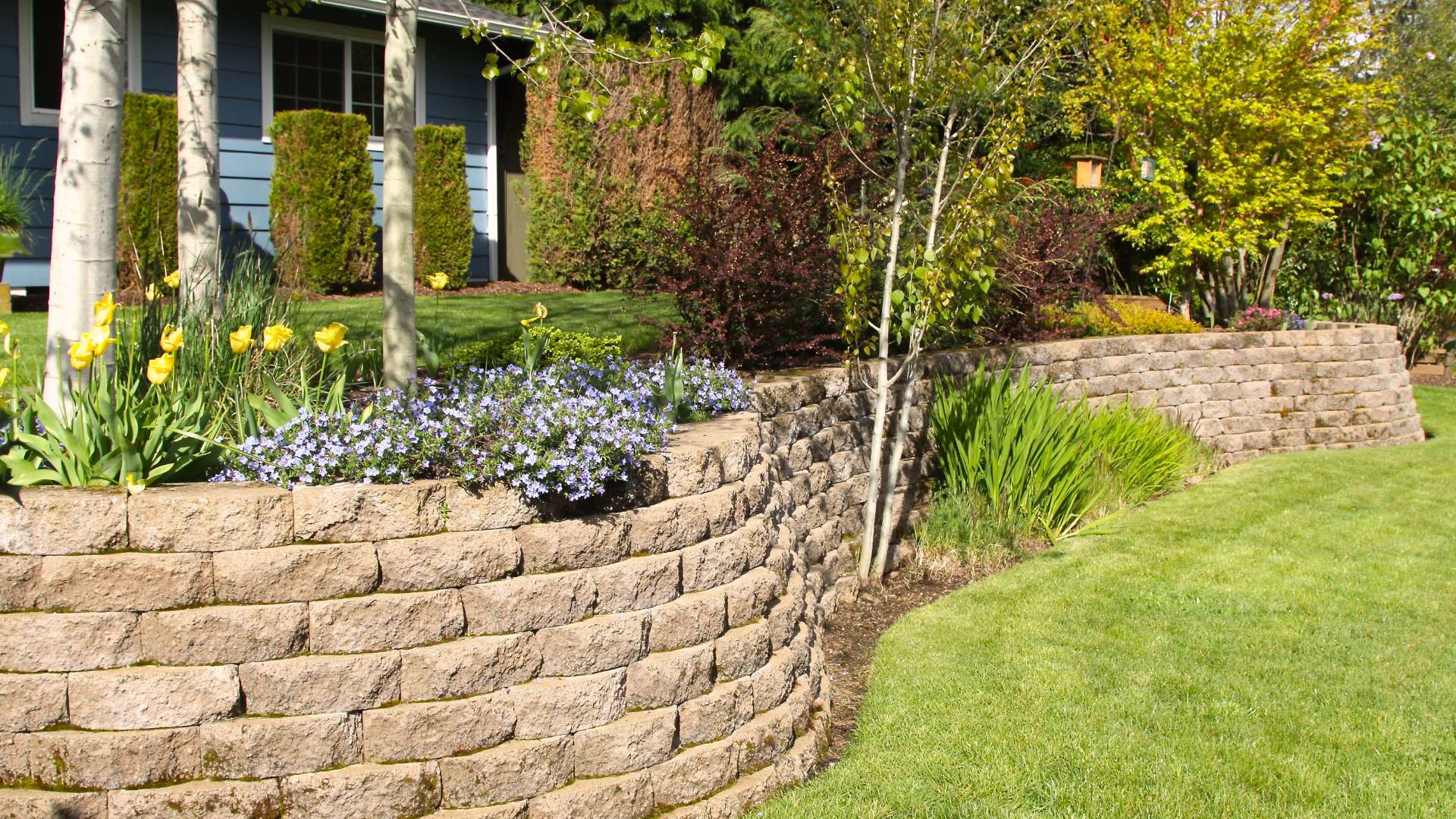 Completed retaining wall installation with landscaped garden beds and lawn in Ridgefield, CT